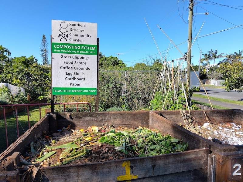A wooden compost bay at Southern Beaches Community garden with a sign listing suitable input materials