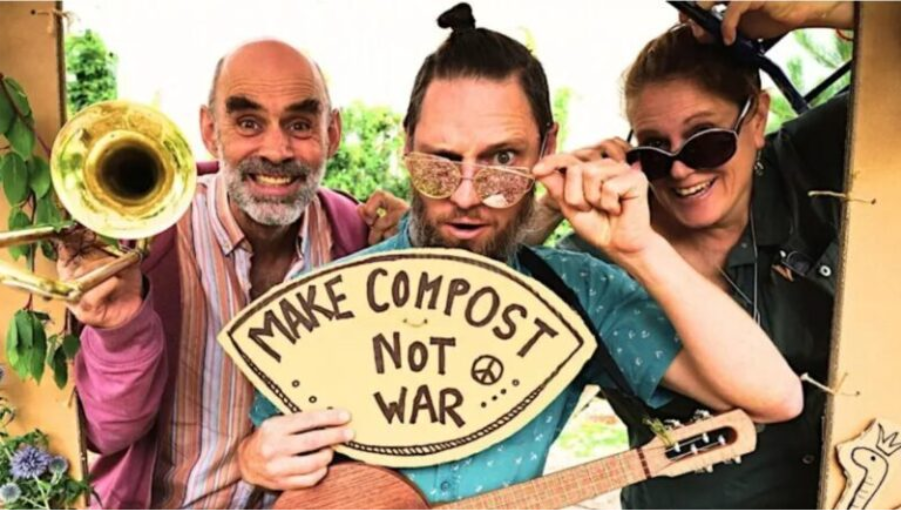 Promo shot of the Formidable Vegetable band holding instruments and a sign reading "Make Compost not War"